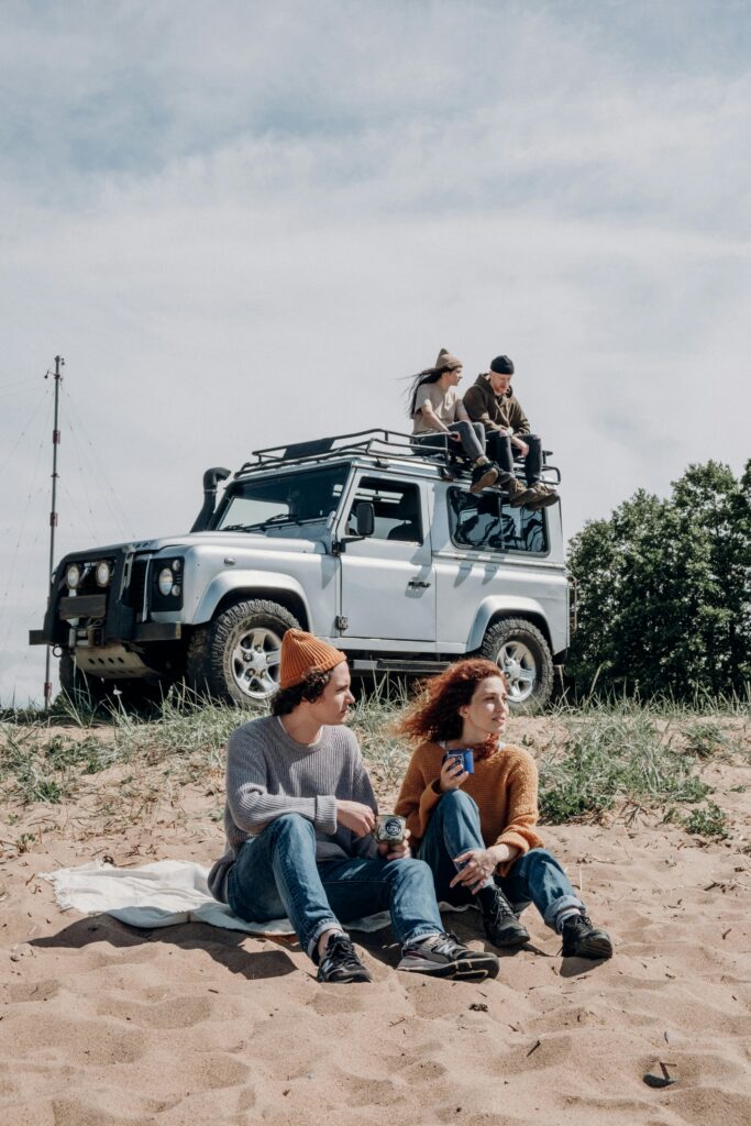 Young friends enjoying a sunny day by the beach with an SUV in the background.